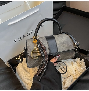 Detail of cylinder bag in dark denim and leather with a gold tennis racket charm
