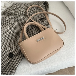Detail of minimalist beige crossbody bag with silver logo plaque on plaid blazer
