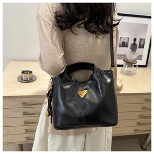 Detail of a black oily leather bucket bag with gold logo and woven bell charm
