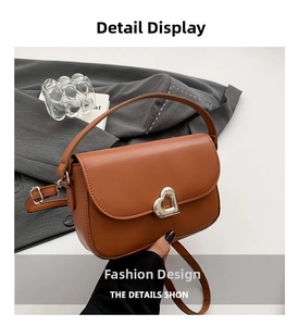 Detail of a brown leather saddle bag featuring a heart-shaped silver metallic buckle lock