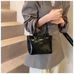 Détail du sac seau noir brillant avec poignées nouées et finitions dorées chic