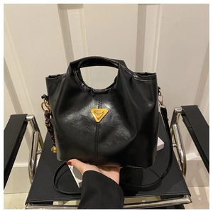 Close-up of black oiled leather tote bag with iconic triangle metal logo and woven charm
