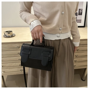 Close-up of minimalist black leather square crossbody bag with dual vintage buckle detail