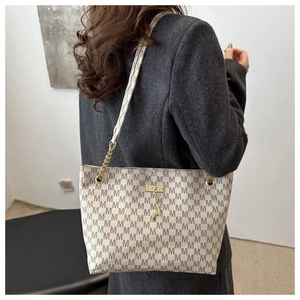 Close-up of beige tote bag featuring M-print pattern, gold chain strap and deer pendant