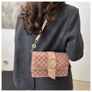 Close-up of pink shoulder bag with dark brown M-pattern and gold circular metal buckle