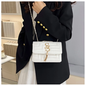 Detail of white quilted crossbody bag with golden S-lock and elegant tassel charm