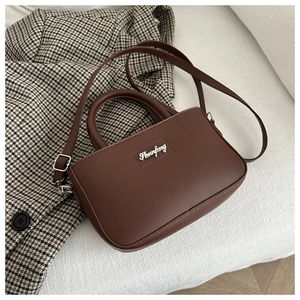 Close-up of matte dark brown leather handbag with silver logo on houndstooth background
