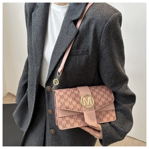 Close-up of pink crossbody bag with brown M patterns and gold metal logo on grey suit