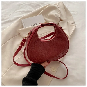 Close-up of wine red crescent bag with crocodile texture and gold metal clasp detail