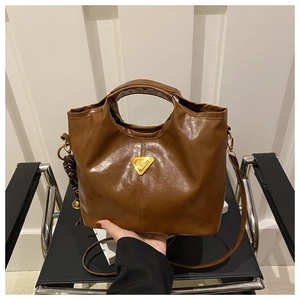 Detail of caramel oil wax leather handbag featuring a golden triangle metal emblem