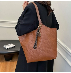 Detail view of brown woven tote bag with fringe tassel and gold tennis racket charm