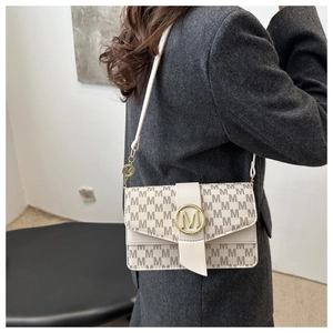 Detail of a minimalist cream crossbody bag with gold M-logo buckle and jacquard pattern