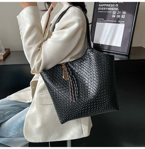 Close-up of black woven tote bag with golden key charm and tassel detail on a model