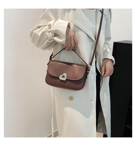 Detailed view of a brown saddle bag with a silver heart-shaped lock on a beige coat