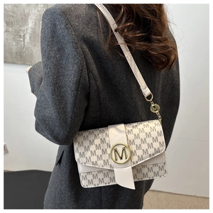Detail of monogram leather crossbody bag with gold M-logo buckle and grey suit outfit