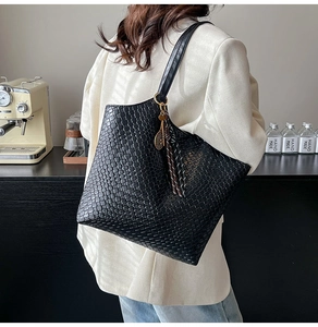 Detail of a black woven tote bag featuring an embossed texture and decorative tassel charms