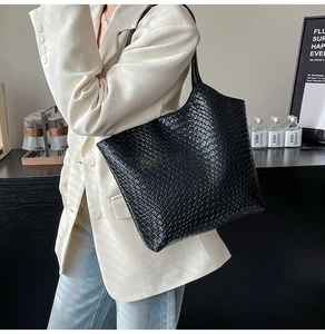 Close-up of black woven leather tote bag texture on model in white blazer