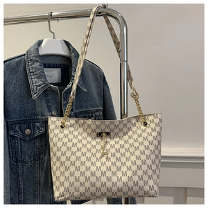 Close-up of monogram tote bag with gold chain strap and deer pendant on blue denim jacket