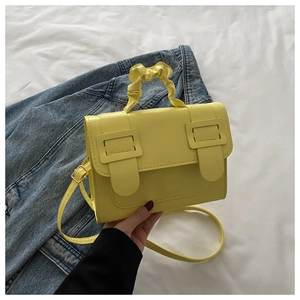 Detail of a bright yellow leather crossbody bag with a ruched handle on denim clothing