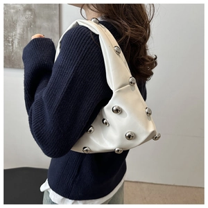 Detail of white underarm bag with silver metallic studs worn by a model in soft light
