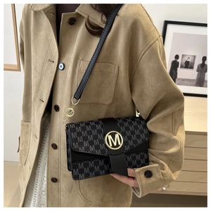 Detail of black monogram shoulder bag featuring a gold M logo buckle and leather strap