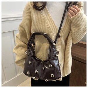 Detail of dark brown ruched shoulder bag with large silver stud rivets on a model