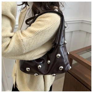 Close-up of deep brown glossy PU underarm bag with silver rivet studs on model's shoulder