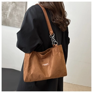 Detail of brown tote bag showing textured fabric, fashion label and metal chain link strap