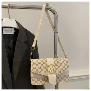 Detail view of cream crossbody bag with brown M-pattern and gold buckle on a suit