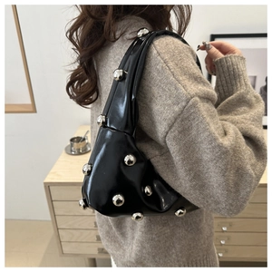Close-up of black patent leather crescent bag with decorative silver metal spheres on shoulder