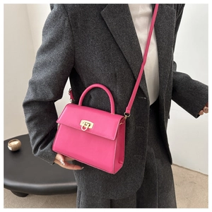 Detail der magenta Trapez-Handtasche mit goldenem Drehverschluss am grauen Blazer-Outfit