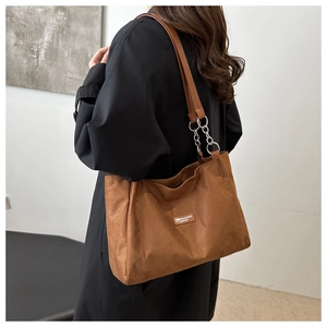 Detail of suede tote bag featuring brown leather and silver metal chain shoulder strap