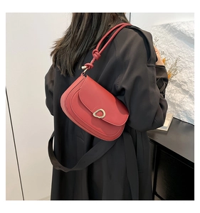 Detail of red leather saddle bag with gold metal buckle and knotted strap on model