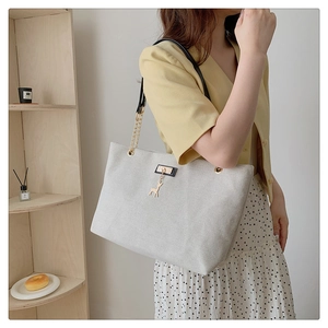Detail of oat beige tote bag with gold deer pendant and metal chain strap on a model