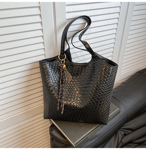 Detail of woven texture tote bag with tennis racket charm on a leather sofa