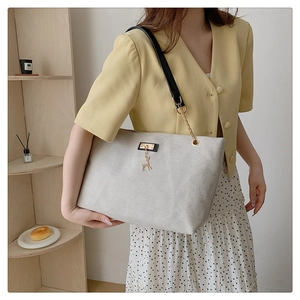 Detail of canvas tote bag featuring gold deer charm and leather chain shoulder strap