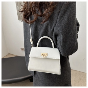 Detailansicht einer cremeweißen Trapez-Handtasche mit goldener Schnalle auf Tweed-Blazer
