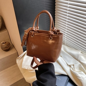 Caramel brown leather bucket bag with knotted handle for women, held against white blazer