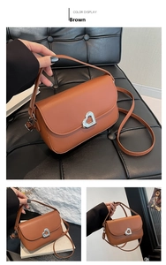 Detail of a brown leather saddle bag featuring a silver heart-shaped metal twist lock