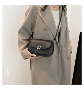 Detail of black leather half-moon bag with gold buckle on beige wool coat