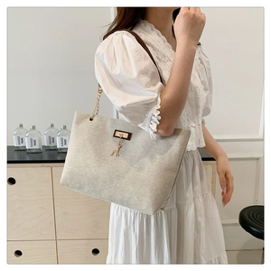 Detail of beige canvas tote bag with brown leather straps and gold metal deer pendant