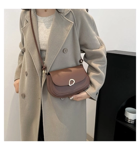 Brown saddle crossbody bag with unique gold hardware worn by model in minimalist setting