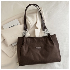 Detail of dark brown suede tote bag with silver chain straps on a white blazer