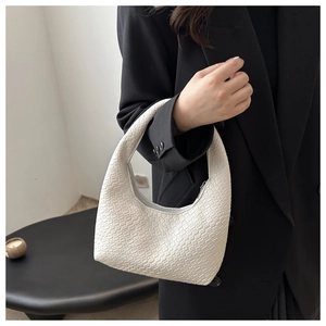 Detailed texture of white woven Hobo bag carried by model wearing a black blazer