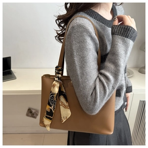 Brown leather tote bag with a decorative silk scarf handle shown in a lifestyle setting