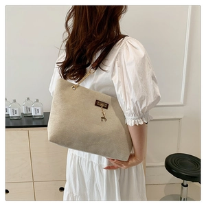 Close-up of oatmeal canvas tote bag with brown leather straps and gold deer charm detail