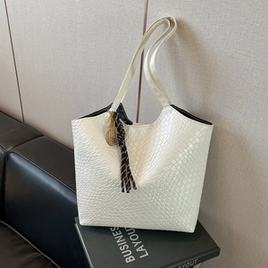 Large woven texture tote bag with striped tassel and gold racket charm on a black book