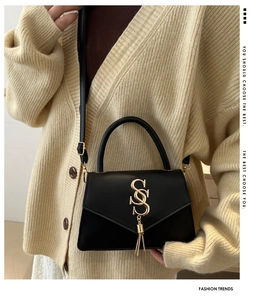 Detail of black leather crossbody bag with gold S-hardware and elegant metal tassel