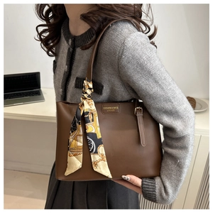 Detailed close-up of brown leather tote bag handle decorated with printed silk scarf