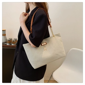 Detail of beige tote bag with gold chain strap and deer charm on a black suit model